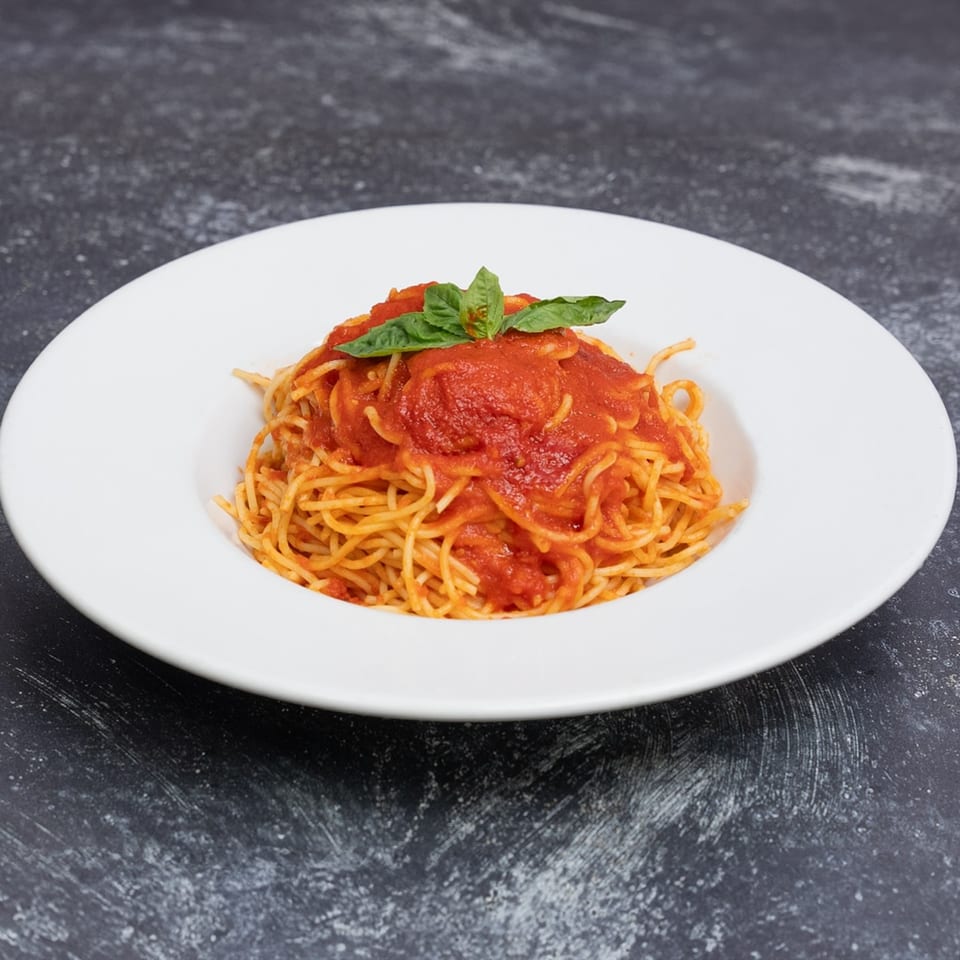 Spaghetti with red tomato sauce and fresh basil leaves in a white bowl on a dark background.